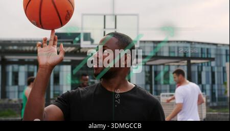 Spinning man wearing black tee twirling orange basketball on finger at outdoor court by metal hoop Stock Photo