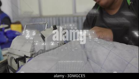 Operating industrial sewing machine, woman guiding quilted fabric in workshop wearing blue jacket Stock Photo