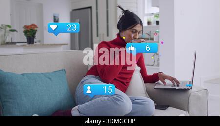 Sipping woman in red sweater, jeans, typing on laptop at home, holding mug checking phone alerts Stock Photo
