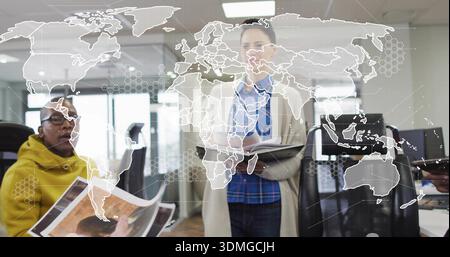 Presenting woman in beige-coat holding folder-and-pen at office with map overlay and prints Stock Photo