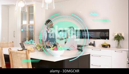 Standing mature couple interacting at kitchen island, man in striped apron, HUD overlay and laptop Stock Photo