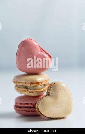 Three heart-shaped macarons are arranged in a stack. The top macaron is pink, while the one in the middle is a light cream color. Stock Photo
