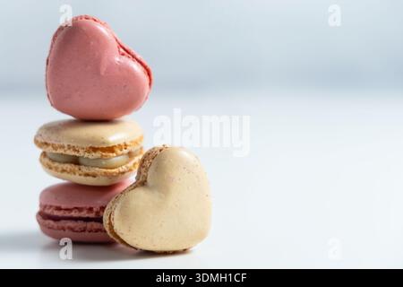 Three macarons are stacked on a white surface, forming a small tower. The top two macarons are heart shaped, one colored pink and the other beige. Stock Photo