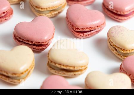A variety of heart-shaped macarons are arranged on a white plate. The macarons come in different colors, mainly pastel pink and cream. Stock Photo