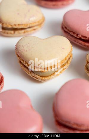 Several heart-shaped macarons are arranged on a plain white surface. The macarons come in shades of pink and beige. Stock Photo