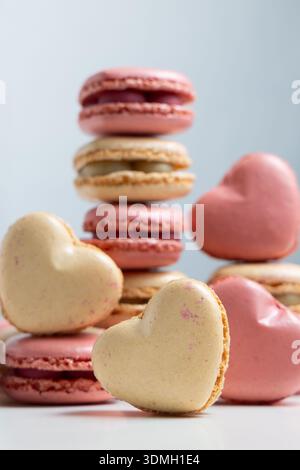 Heart-shaped macarons are placed in various positions on a white surface. Stock Photo