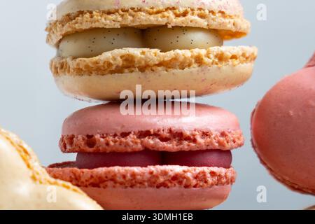 Different types of macarons are stacked on top of each other. The top macaron is light in color and has a smooth surface. Stock Photo