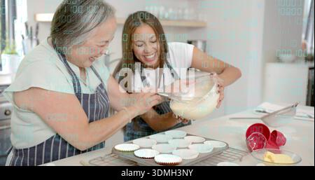 Mixing cupcake batter, mother and daughter in aprons stirring with whisk, holding bowl in kitchen Stock Photo
