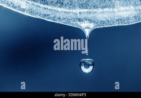 A drop of water is falling from a ice surface. The water is clear and the drop is small Stock Photo