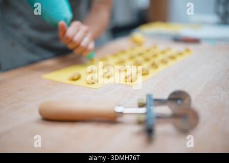 Homemade ravioli preparation using a piping bag and pasta cutter on a wooden table Stock Photo