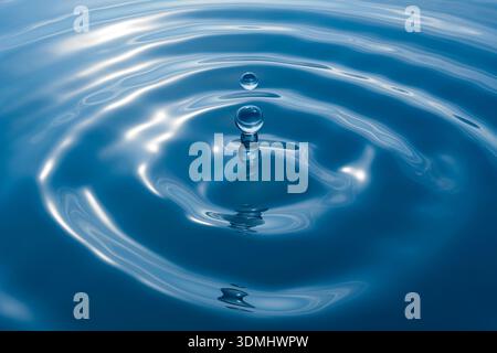 Water Droplet Impact Forming Expanding Ripples on Blue Liquid Surface. High quality photo Stock Photo