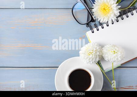 Notebook with an open blank page, glasses, pen, white cup with black coffee, dahlia flowers. Morning coffee cup. Stock Photo