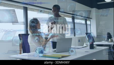 Talking two coworkers in business casual gesturing over laptop in office with mug, showing UI Stock Photo