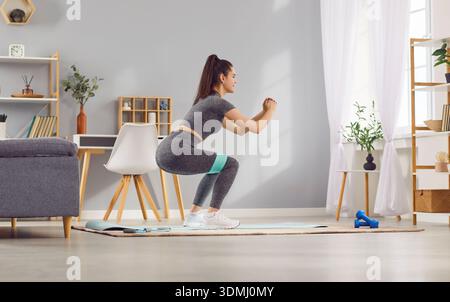 Woman Doing Squats With Fitness Band In Home Gym Stock Photo