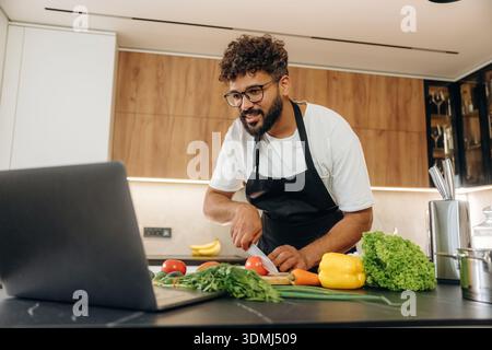 Slicing the vegetables. Handsome man is preparing food on the kitchen. Stock Photo