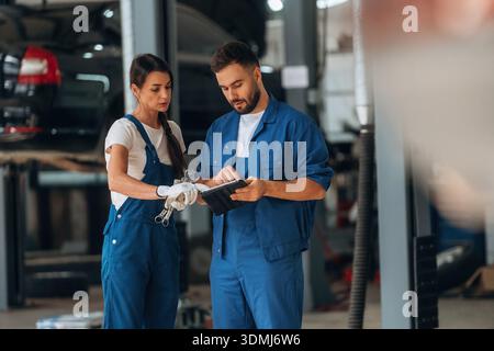 Digital tablet is in hands. Auto repair shop employees are working together. Man and woman. Stock Photo