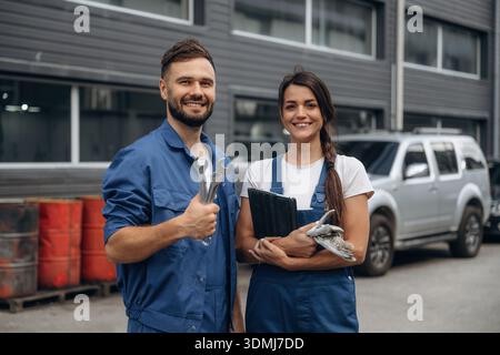 Cheerful male and female mechanics are standing outdoors together. Stock Photo