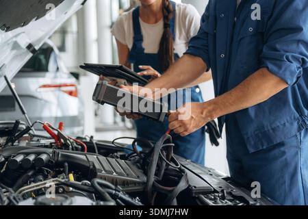 Particle close up view of male and female mechanics that are repairing the car. Stock Photo