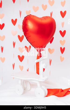 Red heart-shaped balloon on white background with decorative hearts. Valentines Day symbol, love, romance, minimal festive concept Stock Photo