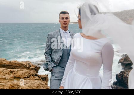 Bride and groom in wedding attire posing on rocky coastline Stock Photo
