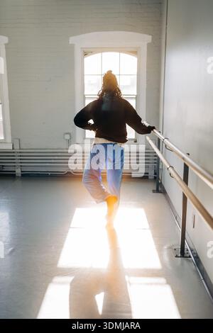 Dancer practicing ballet barre exercise in sunlit studio Stock Photo