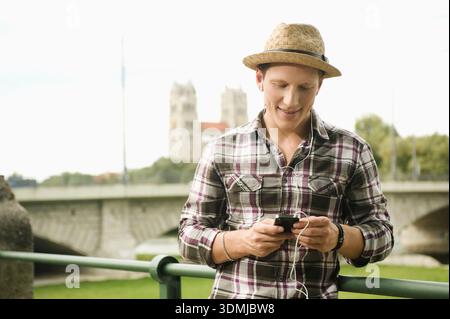 Young man with straw hat texting on his smartphone. Stock Photo