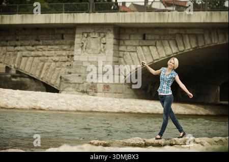 Young woman balancing on wall by the river  with arms outstretched. Stock Photo