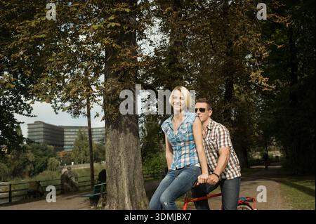 Happy young couple sitting on bicycle in urban park Stock Photo