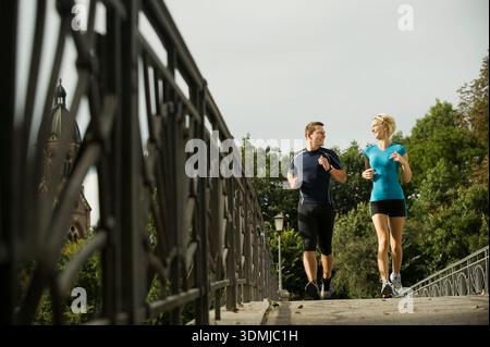 Young couple jogging together on urban bridge and smiling each other Stock Photo
