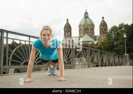 Athletic young woman doing push ups on pedestrian bridge in city Stock Photo