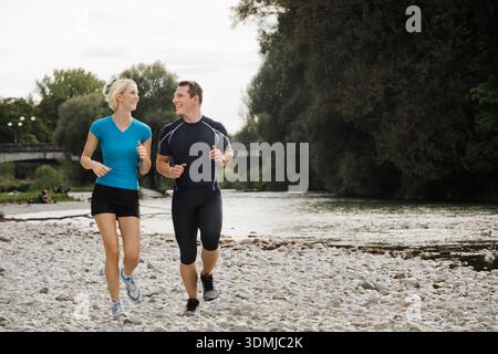 Athletic couple jogging together on rocky riverbank in the city Stock Photo