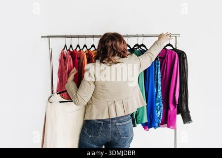 Woman organizes professional attire in rainbow order on hangers Stock Photo