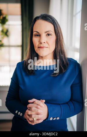 Professional woman standing with clasped hands by window Stock Photo