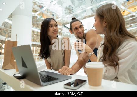 Diverse friends talking and using laptop in shopping mall Stock Photo