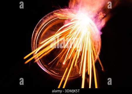 Exothermic alkali metal reaction. A piece of sodium skitters across water in a petri dish, creating a starburst of orange sparks (long exposure). Stock Photo