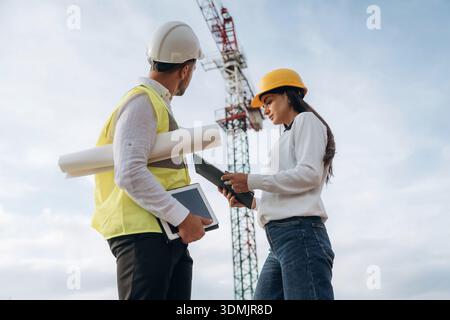 Man and woman, construction site workers are against crane, communication. Stock Photo