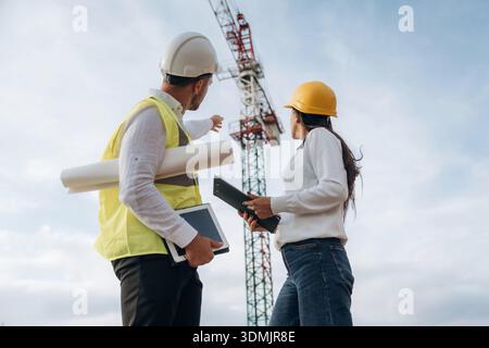 Man and woman, construction site workers are against crane, communication. Stock Photo