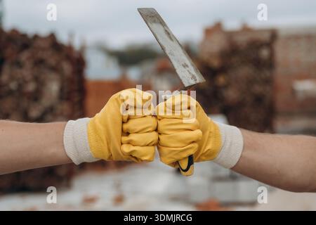 Side view of two hands of builders on construction site that are knocking the fists, conception of teamwork, unity. Stock Photo