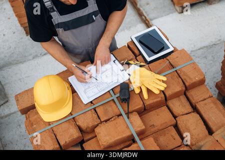 Working on a plan, paper on the bricks. Close up view of builder that is on the construction site. Stock Photo