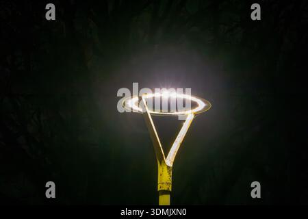 Modern street lamp with circular LED light glowing in the dark night environment. Minimalist urban scene with strong contrast and futuristic design. Stock Photo