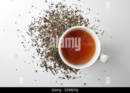 Hot infusion in a white ceramic cup on a white table with dried medicinal herbs. Top view. Stock Photo