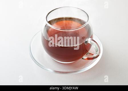 Hot infusion in a glass cup with saucer isolated on white table. Elevated view. Stock Photo