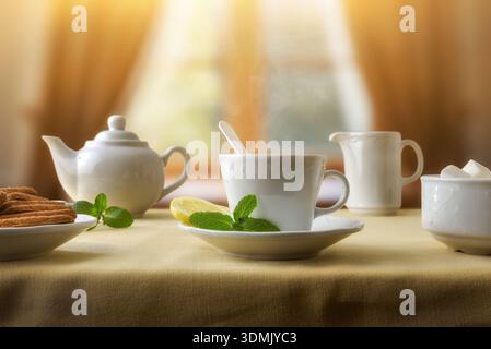 Freshly served mint and lemon tea on a table with a brown tablecloth and ceramic glassware with cookies in a tea room. Front view. Stock Photo