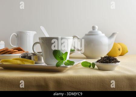 White ceramic tea set with ingredients on a table with a tablecloth and isolated white background. Front view. Stock Photo