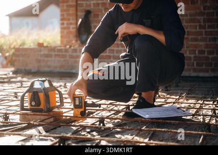 Sitting and using leveling tool. Builder is working on construction site, unfinished building. Stock Photo