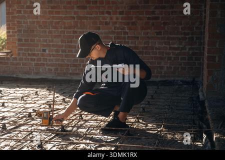 Sitting and using leveling tool. Builder is working on construction site, unfinished building. Stock Photo