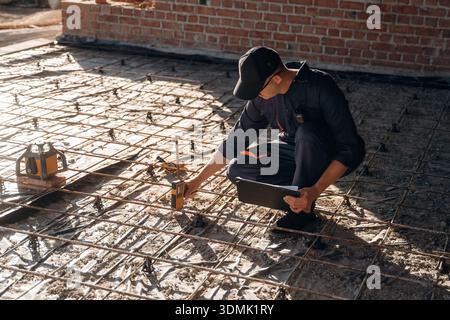 Sitting and using leveling tool. Builder is working on construction site, unfinished building. Stock Photo