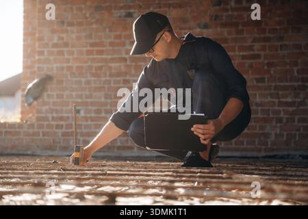Sitting and using leveling tool. Builder is working on construction site, unfinished building. Stock Photo