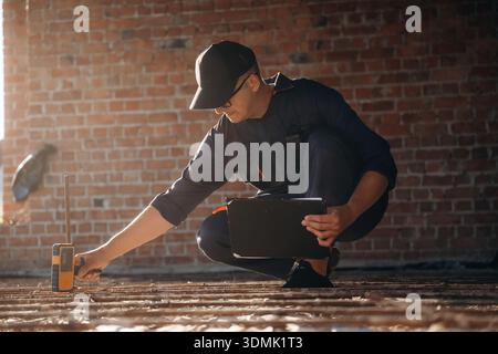 Sitting and using leveling tool. Builder is working on construction site, unfinished building. Stock Photo
