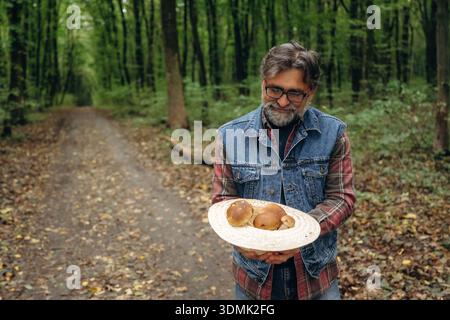In the hat, holding in hands. Mushroom picking. Man is in the forest at daytime. Stock Photo